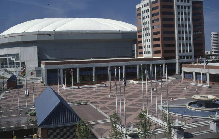 A view of a large plaza with several flags placed throughout. A domed building is in the background.