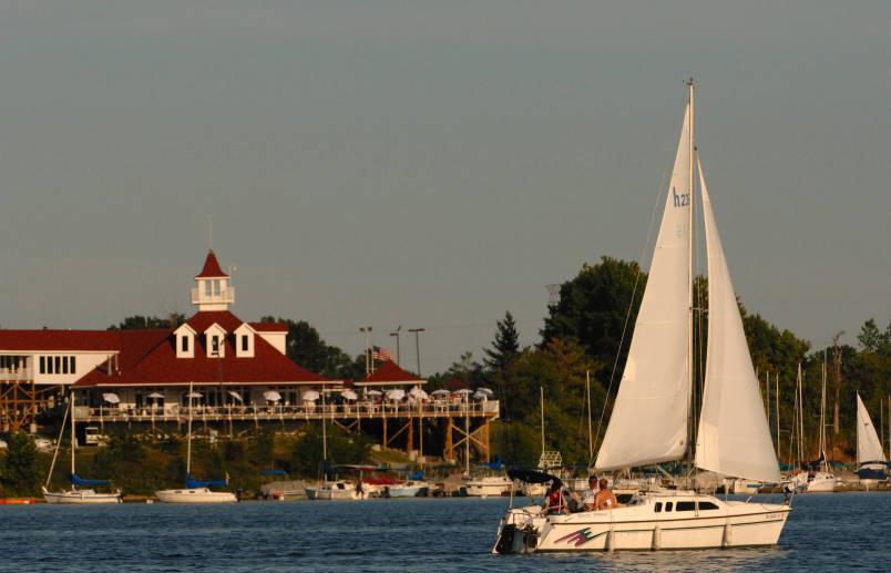 A sail boat floats on the reservoir. A large building is on the banks in the background.