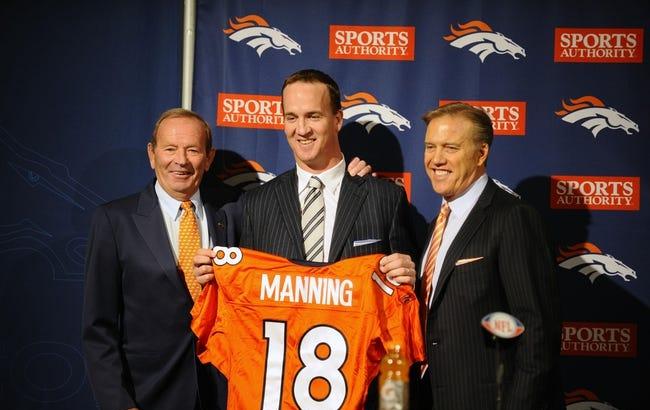 Peyton Manning holds up an orange jersey. Two men stand next to him.