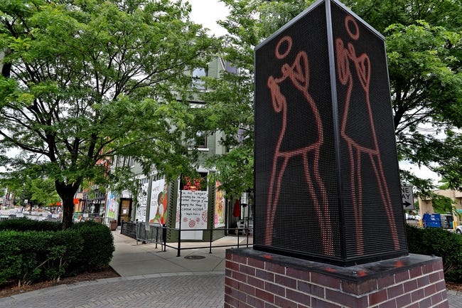 A sculpture with a brick base and panels with a line figure of a woman dancing. 