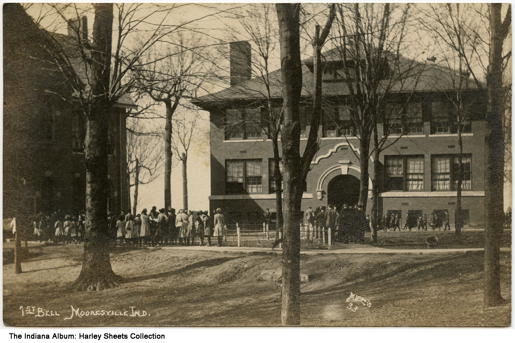 Groups of people stand outside a brick, three-story school building.