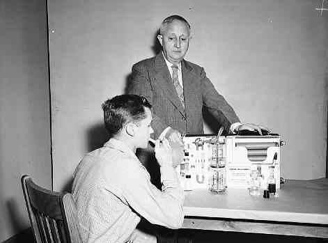 A young man breaths into a device. Another man watches.