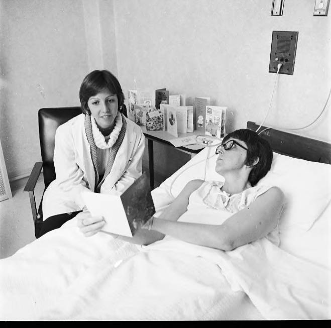 A woman sits in a chair next to another woman in a hospital bed.