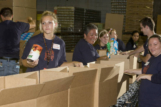 Young adults place food goods into boxes. 