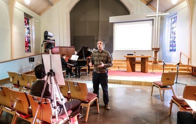 A man stands in an empty church. He is giving a sermon in front of a camera.