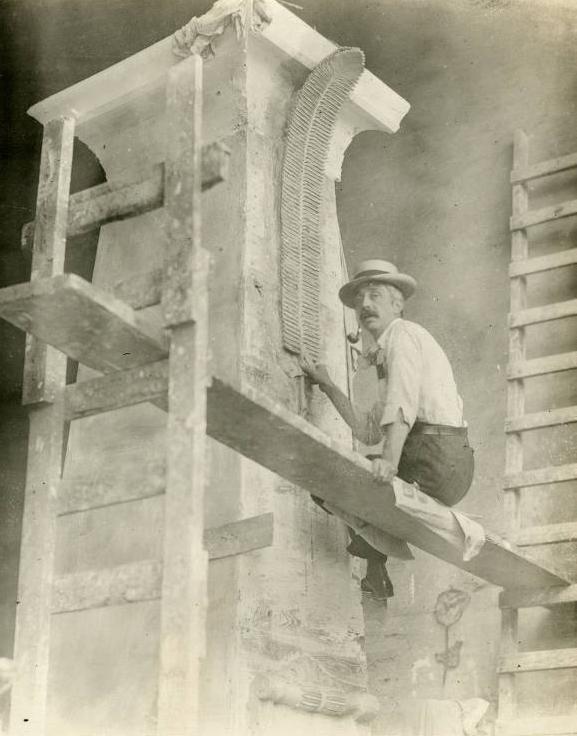 Steele sits on scaffolding as he works on carving stone.