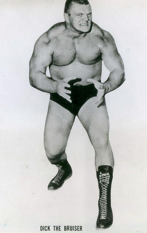 A man wearing black briefs and boxing boots is striking a threatening pose.