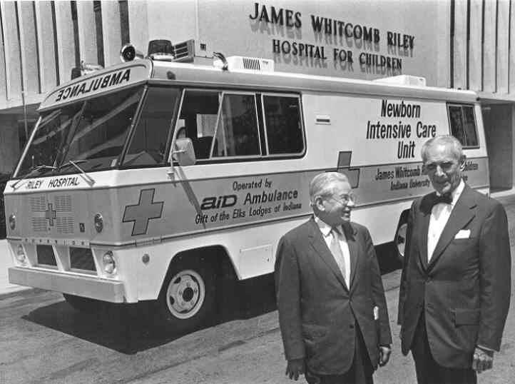 Two men stand outside of an ambulance.