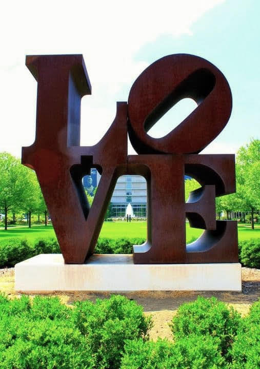 The sculpture, in which the letters "L" and "O" rest on the "V" and "E" in a square formation, sits in a tree-lined plaza.