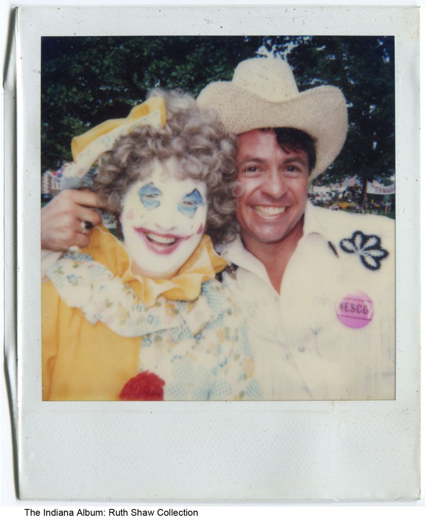 Polaroid photo of a man in a cowboy hat with his arm around the shoulders of a woman in clown make-up and costume.