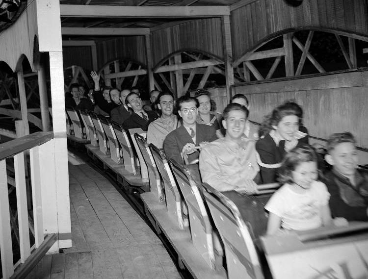 People sit in a roller coaster car as it leaves the station.