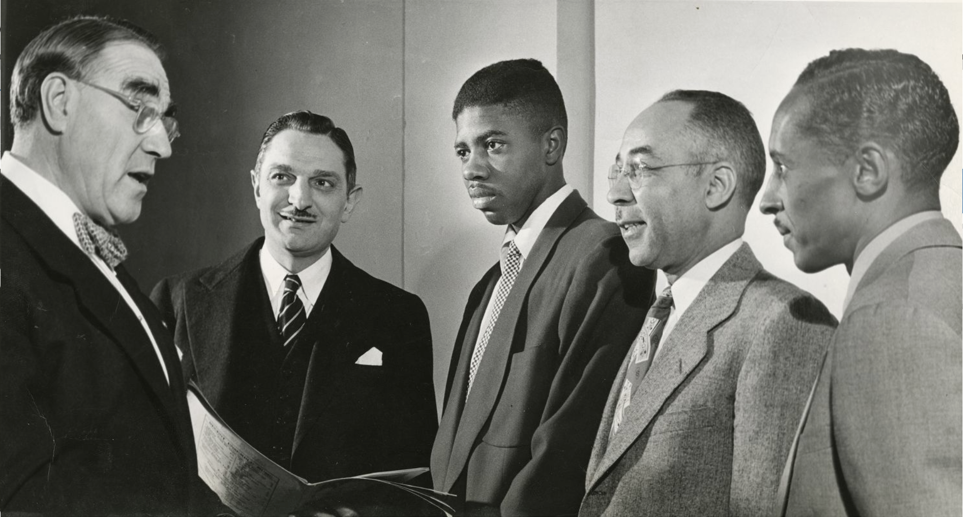 A man is talking to a group of four other men, one of which is a young Rozelle Boyd. 