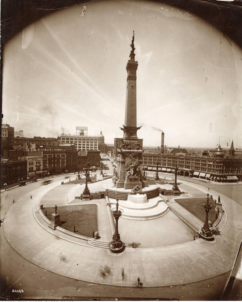 Sweeping aerial view of the west side of Monument Circle showing the Soldiers and Sailors monument in the center  and buildings in the background..