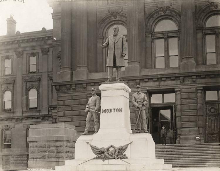 A statue of a man is set on a pedestal. Statues of two Civil War soldiers are set on either side of the man on pedestals below him. 