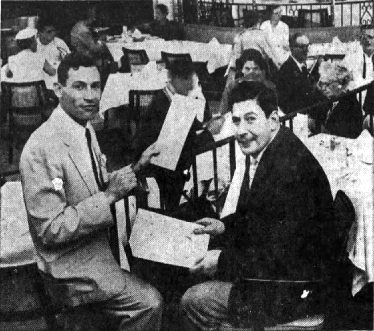 Two men sit at a restaurant table. One man is holding a menu. 