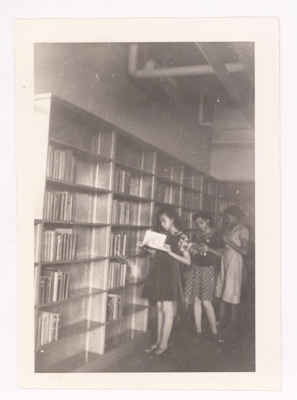 Several people are looking at books that were taken off a wall lined with book shelves.