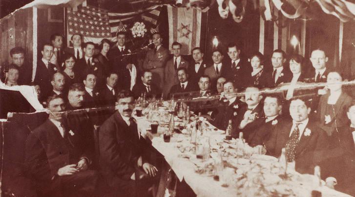 A group of people are standing behind and seated around a long table.
