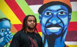 Artist Israel Solomon stands in front of a mural he painted on boarded windows in the 300 block of Mass Ave in Indianapolis, 2020