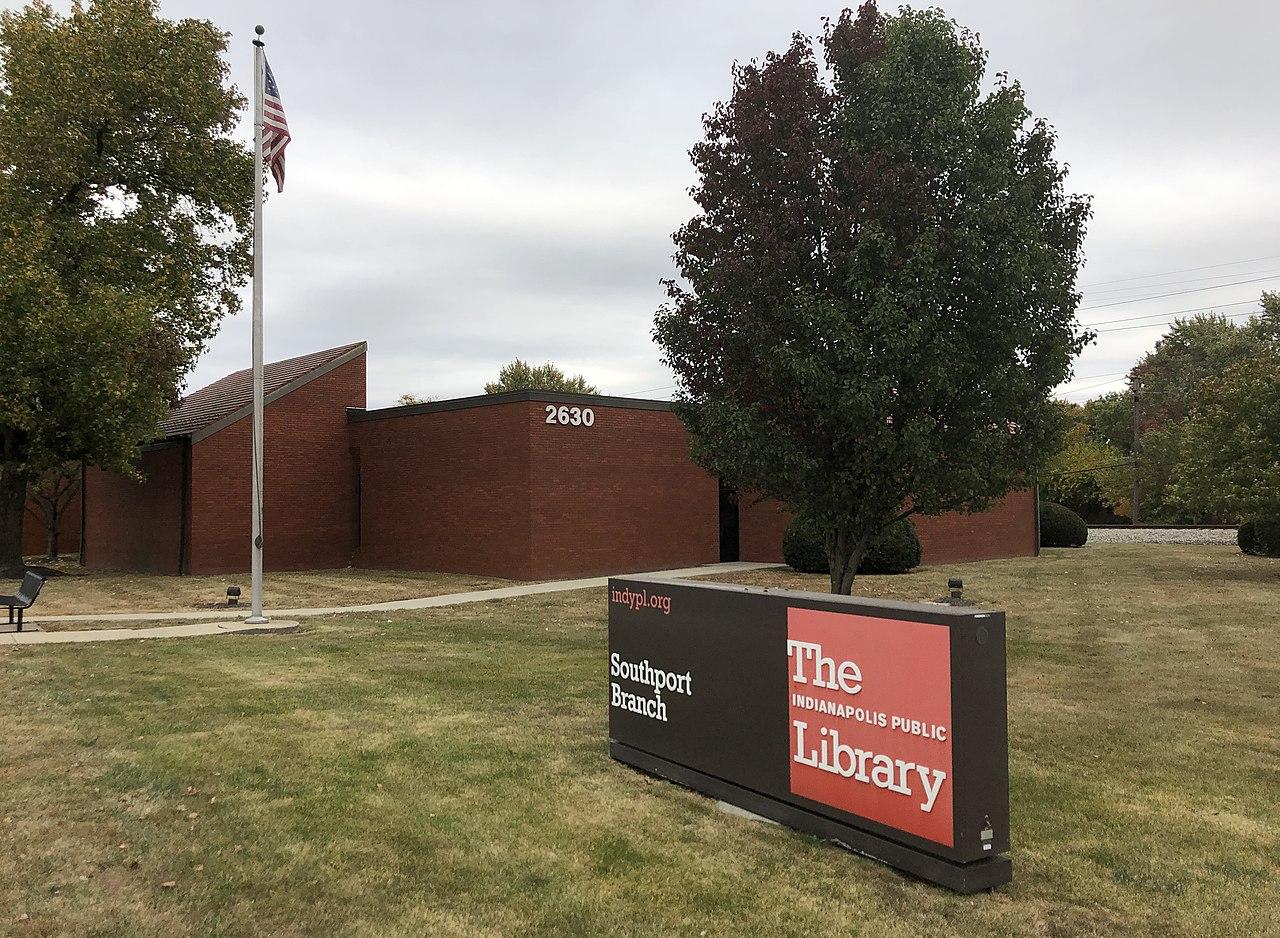 Exterior view of a library building with a sign on the lawn that reads