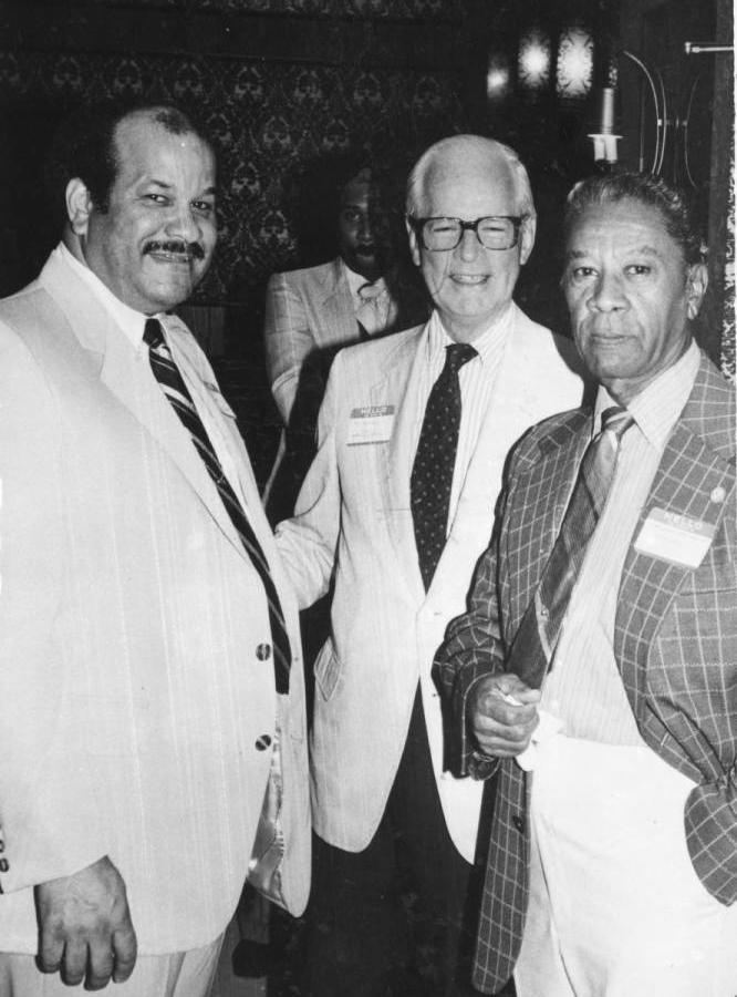 Three men wearing suit coats and ties stand together.