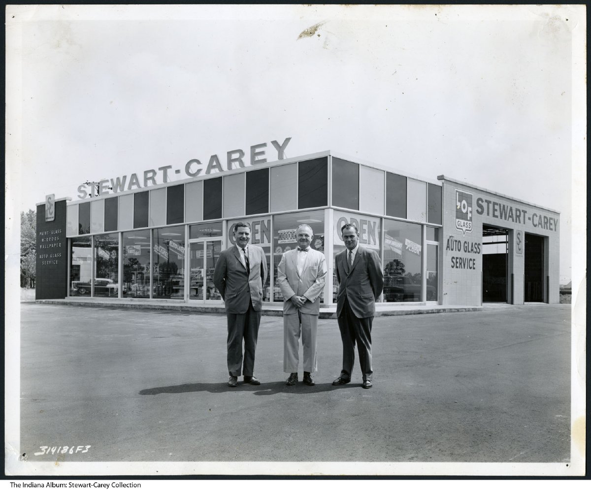 Three men stand outside of the Stewart-Carey auto repair shop. 