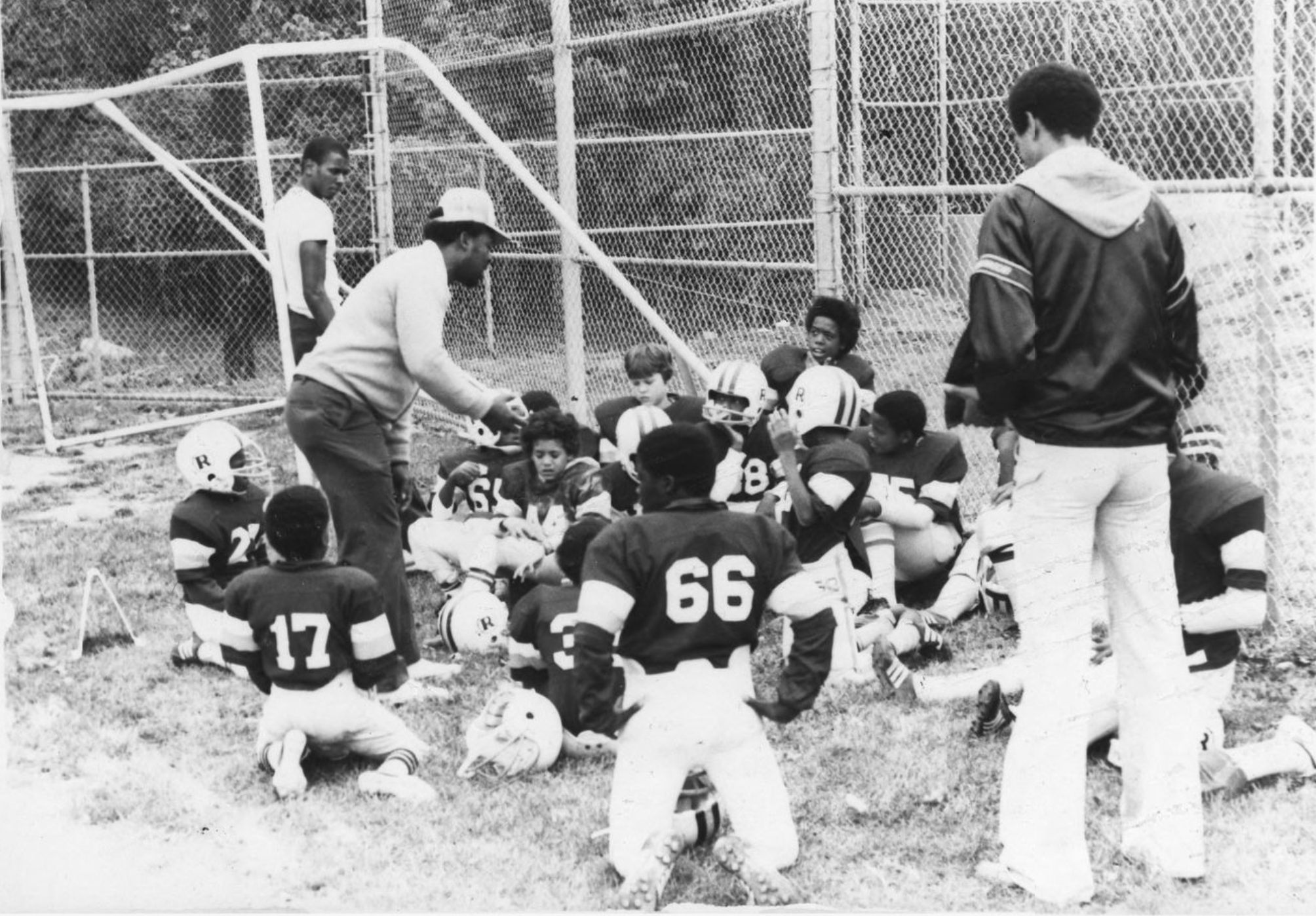 A group of children in football uniforms gather to listen to their coach.