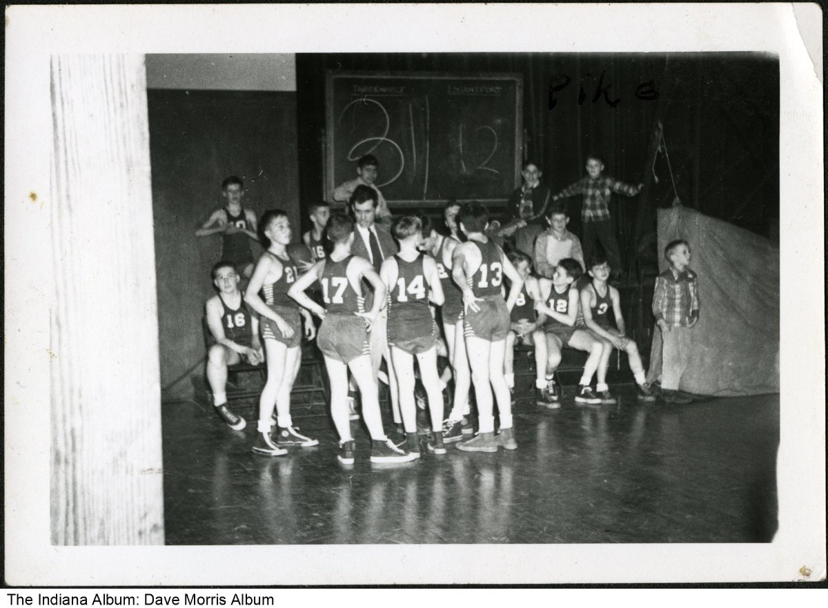 A group of boys in basketball uniforms are gathered around their coach.