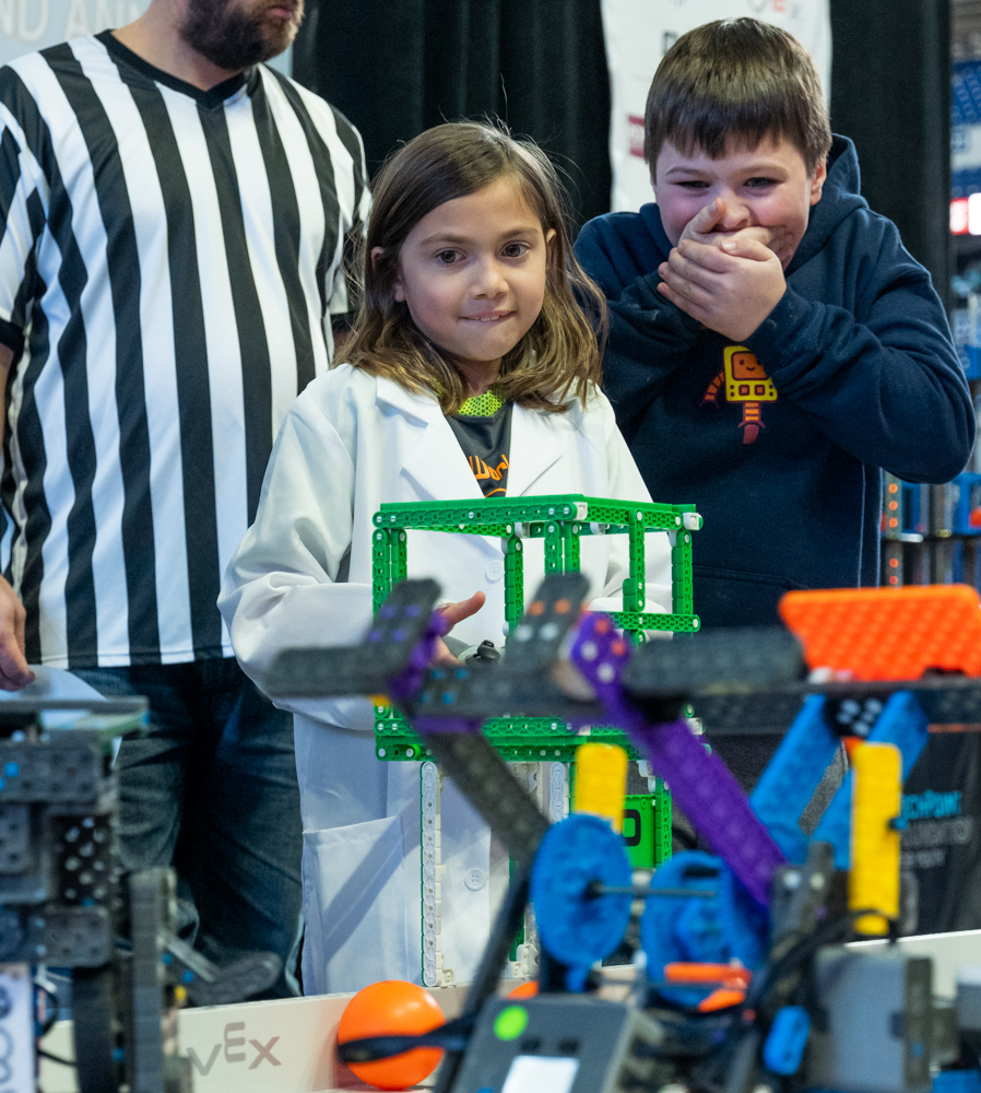 Two children look at robots. A referee stands in the background.