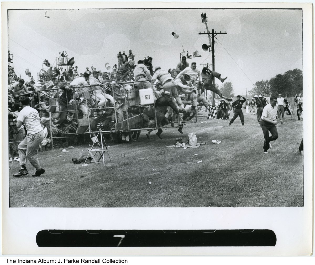 People run to avoid being hit by a scaffolding that is falling. The scaffolding is filled with people.