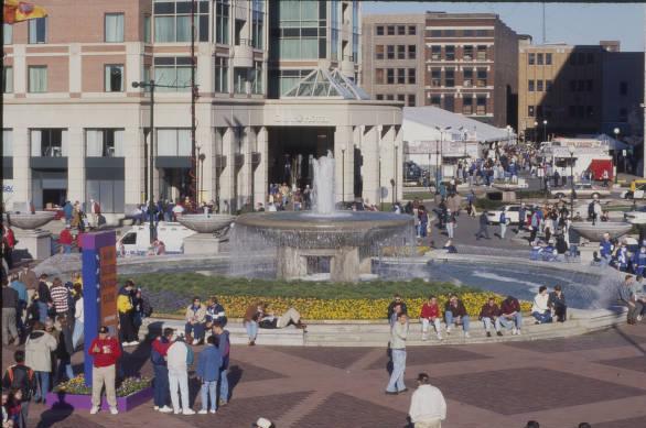 People mill about a large circular fountain. 