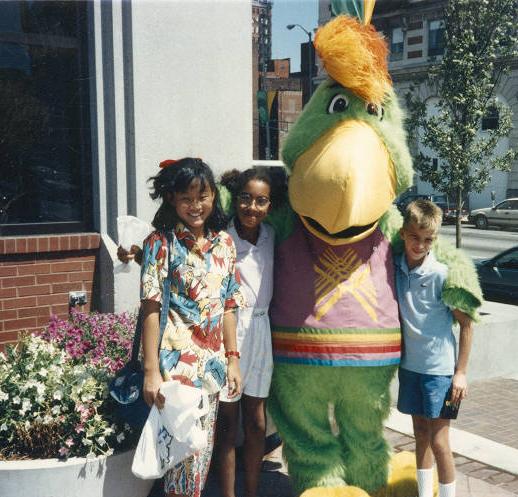 Three children stand next to a parrot mascot. 