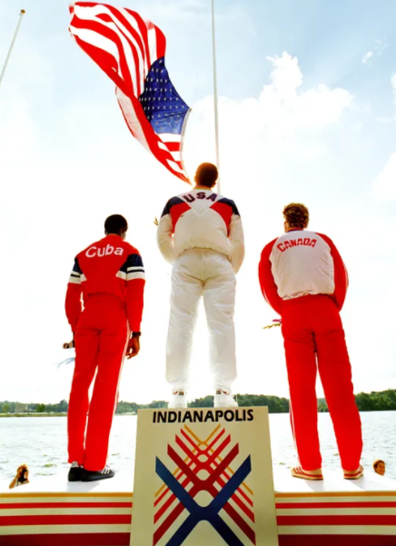 A view showing the back of three men standing and looking at a flag.