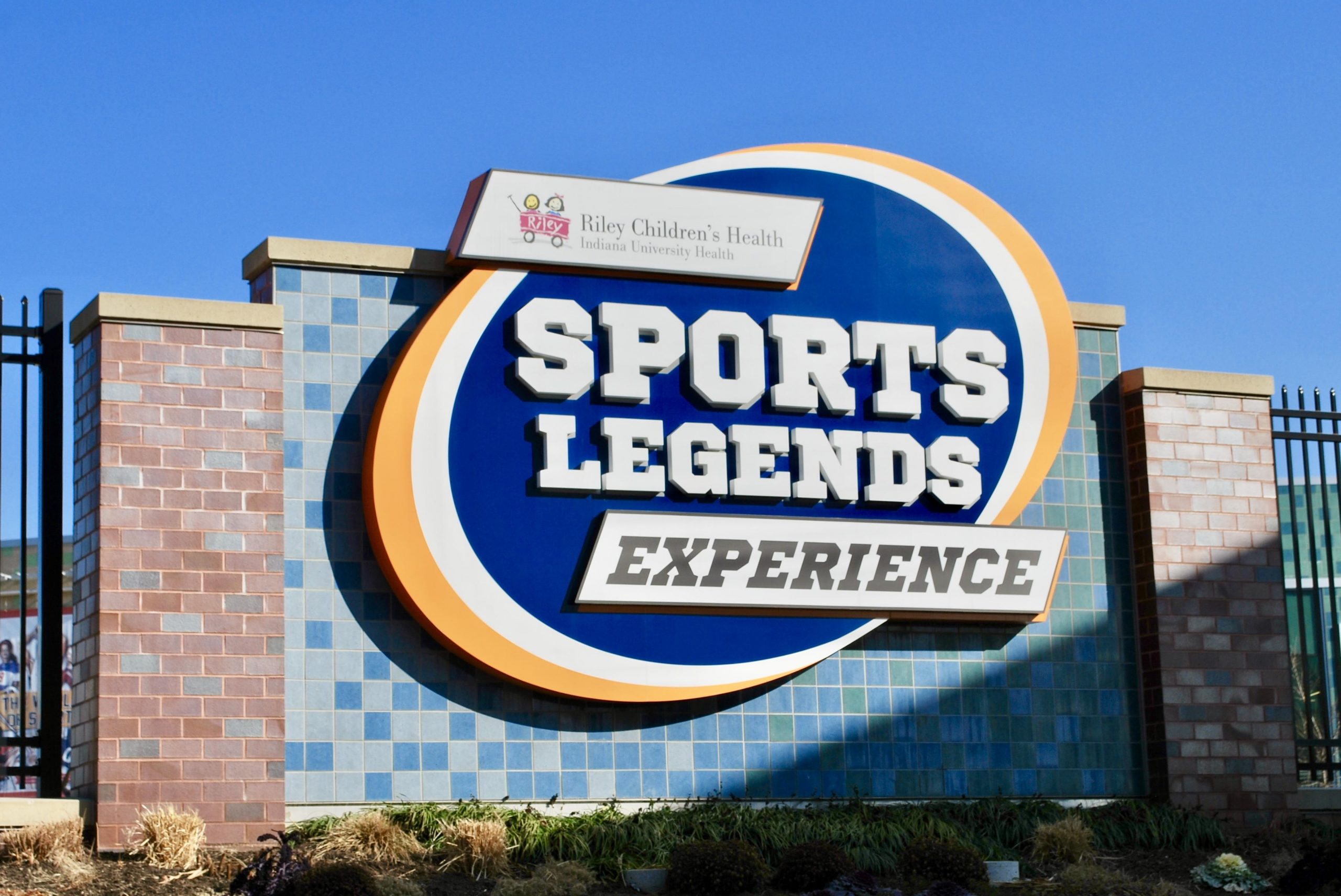 A sign that says "Sports Legends Experience" and a smaller sign attached with the Riley Children logo.