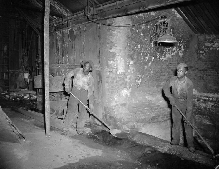 Two men holding shovels are working in a basement-like room.