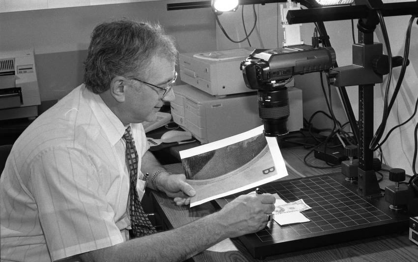 A man examines money under a microscope.