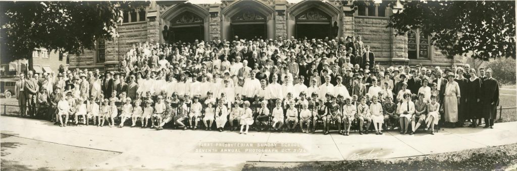 A large group of people stand together on the front steps of a church. 