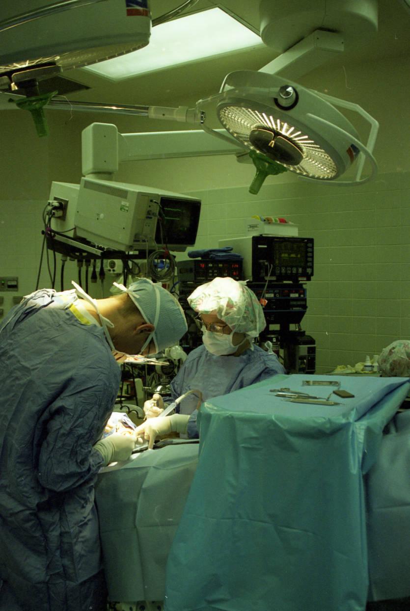 Two medical professionals are in an operating room and working on a patient.