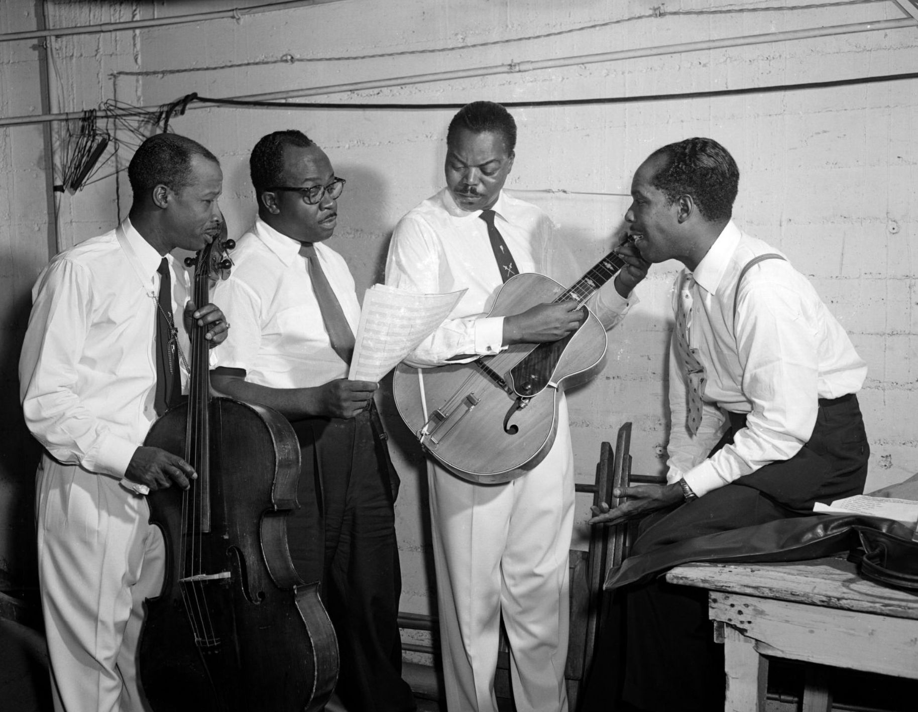 Four men stand together and look at sheet music.