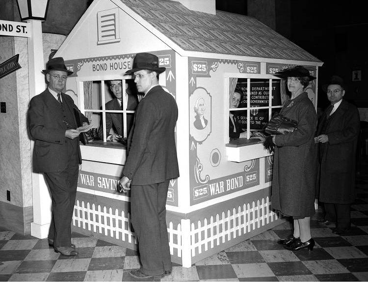 Two people work inside a bond booth. Four people stand on the outside of the booth.