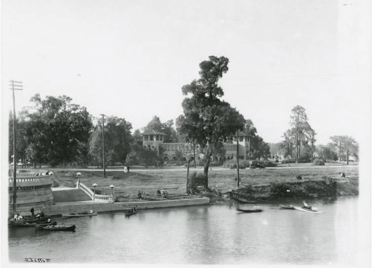 A river bank with canoes in the water. A large park shelter is in the background.