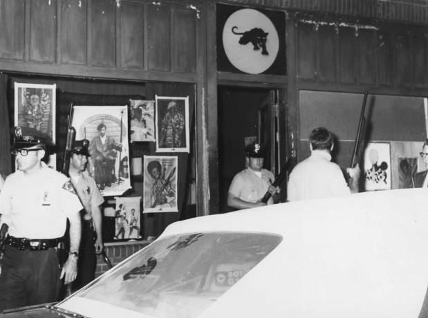 Armed white police stand outside Black Panthers headquarters.
