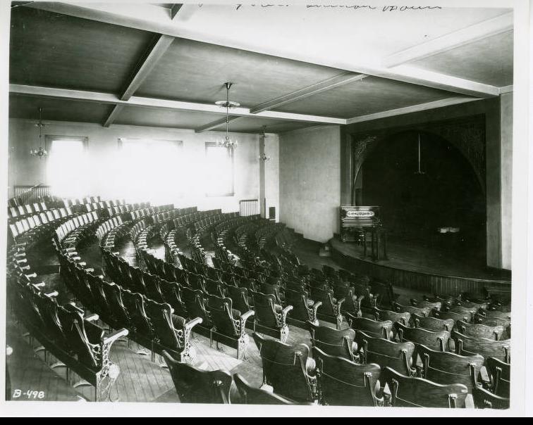 An auditorium showing rows of chairs and a stage with a piano.
