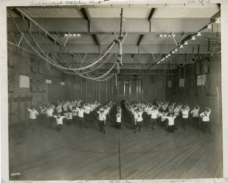 A group of young women in the middle of a workout in a large gymnasium. 