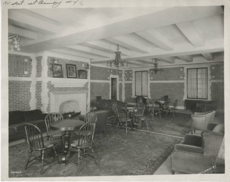 A large room with brick walls and a fireplace. Two large rugs cover the floor and the room is strewn with small tables, chairs, and couches. 
