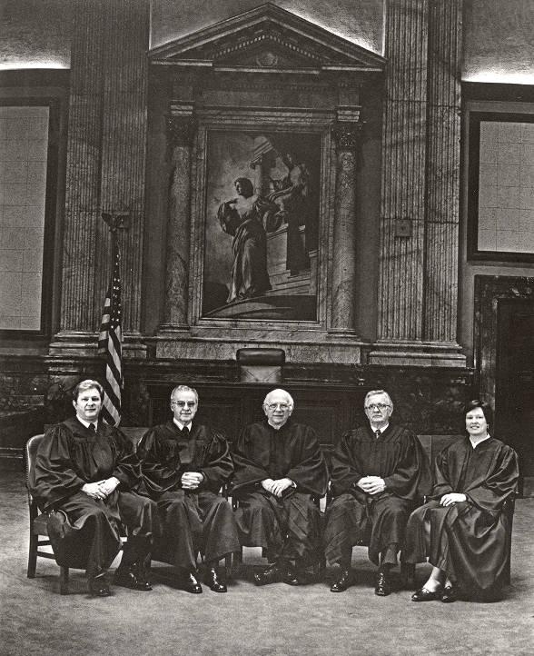 Five judges in full regalia sit in a large room. 