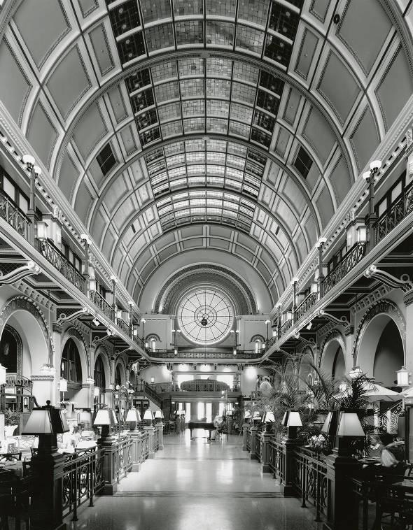 A view down a hall within Union Station. A curved, ornate ceiling covers the hall. Restaurant and Bar seating lines the sides of the space and at the end of the hall is a woman playing on a grand piano.