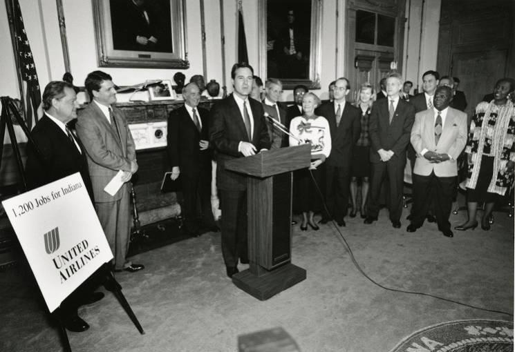 A man stands behind a podium. Several people are gathered behind him.