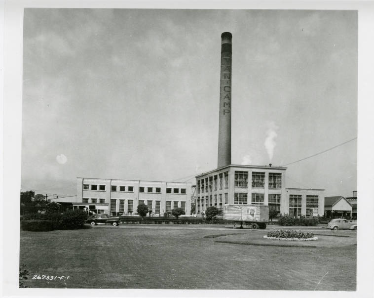 A large factory building with a single tall smoke stack. 