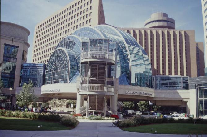 The structure is a seven-story glass dome with glassed-in wings extending to buildings on either side of it. It sits above a street intersection.