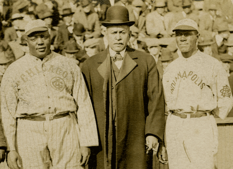 Two men in baseball uniforms stand on either side of another man.